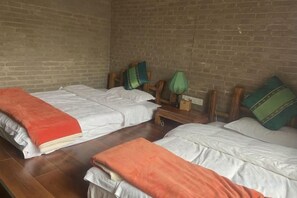 A room with two beds, a brick wall, and a small table with a lamp. - Huayutang Renwen Inn (Luoping)