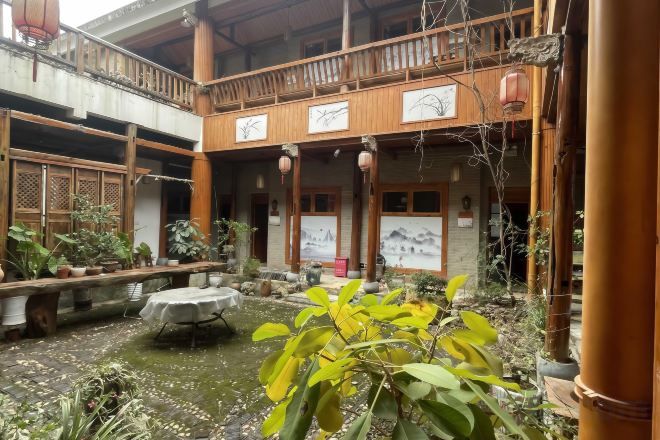 A traditional courtyard with a wooden balcony, potted plants, and a small water feature.