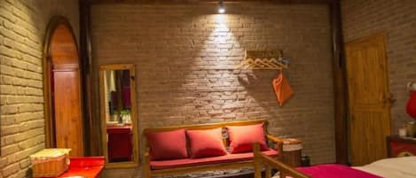 A room with a brick wall, a wooden bench, a bed, and a small table.