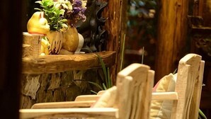 A wooden chair with a cushion, a rustic wooden shelf with a vase of flowers, and a stone wall. - Huayutang Renwen Inn (Luoping)