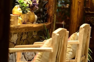 A wooden chair with a cushion, a rustic wooden shelf with a vase of flowers, and a stone wall.