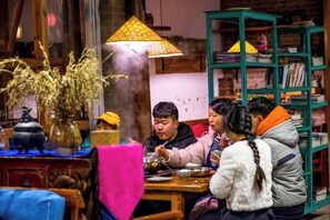 A group of people dining at a table with a traditional lamp and a bookshelf in the background. - Huayutang Renwen Inn (Luoping)
