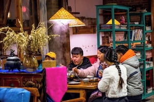 Un grupo de personas cenando en una mesa, con una lámpara tradicional y una estantería al fondo.