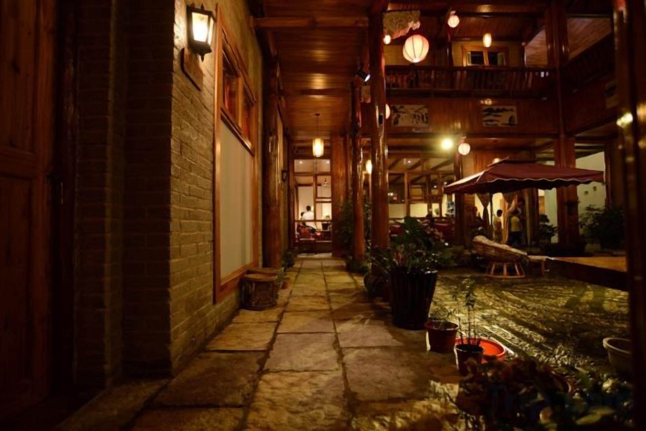 A corridor with wooden walls and a stone floor, leading to a dining area with tables and chairs.