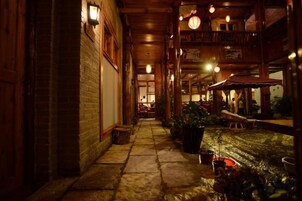 A corridor with wooden walls and a stone floor, leading to a dining area with tables and chairs.