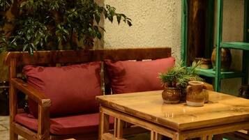 Eine hölzerne Bank mit roten Kissen, ein kleiner Holztisch mit einer Vase und Pflanzen sowie ein grünes Regal mit Gegenständen.