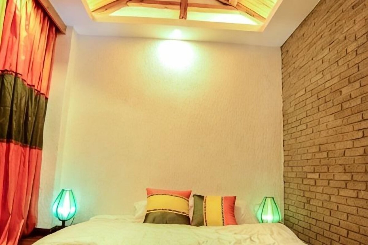 A room with a bed, two bedside lamps, and a brick wall.