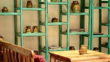 A room with a wooden table and chairs, a bookshelf with ceramic pots, and a wall with shelves.