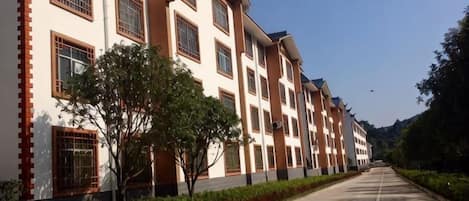 A multi-story building with a long, straight driveway and a row of windows on the ground floor.