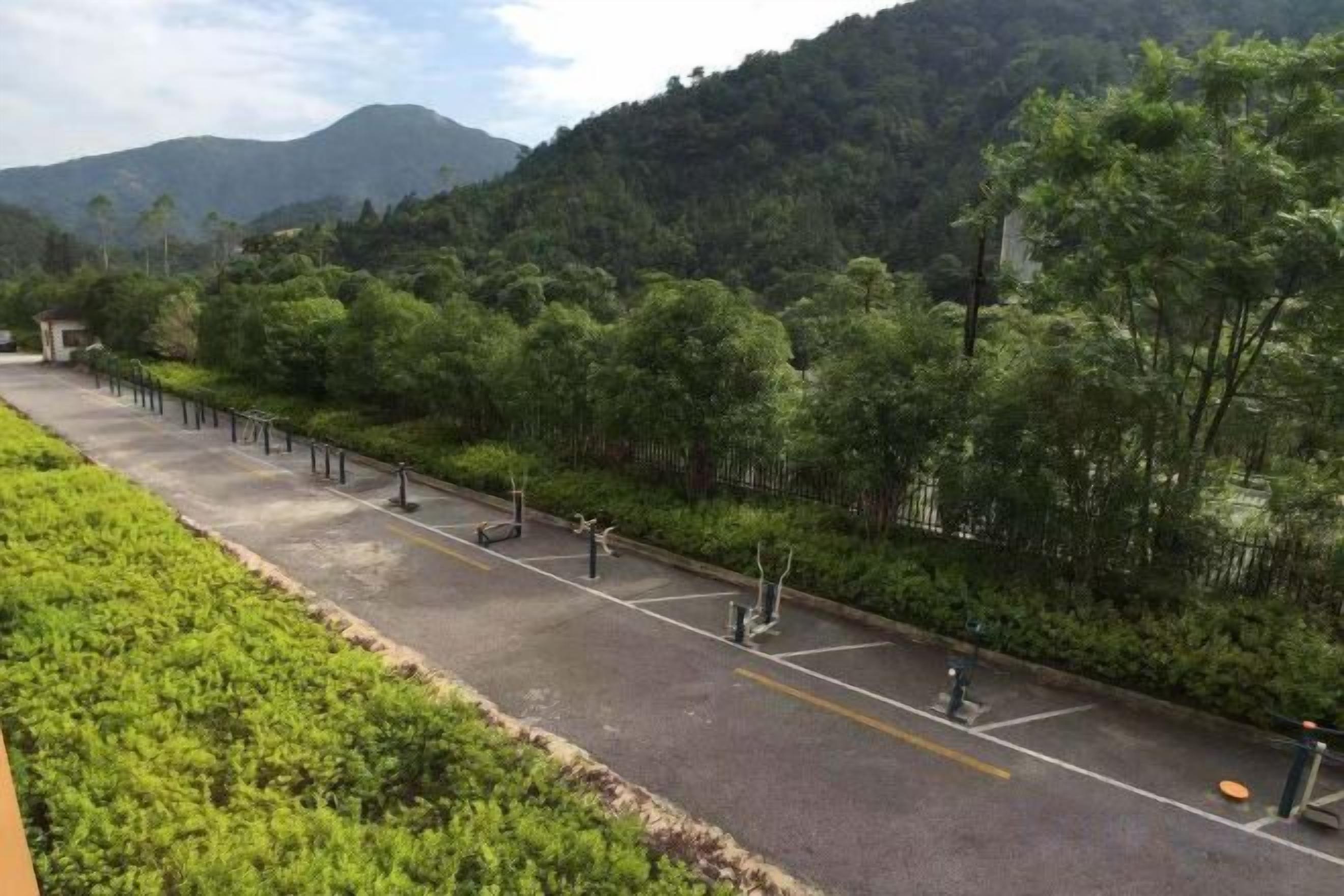 A paved pathway with a fence on one side and a forested hillside on the other.