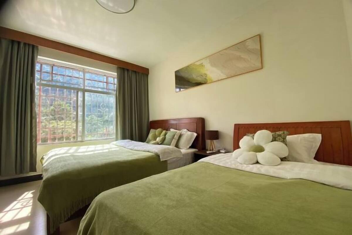 A hotel room with two beds, a large window with curtains, a painting on the wall, and a nightstand with a lamp.