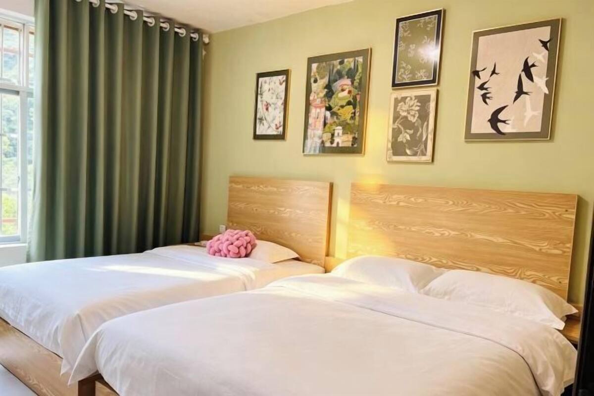 A room with two beds, a green curtain, and framed artwork on the wall.