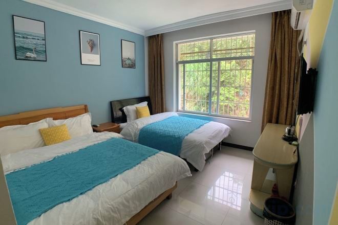 Habitación de hotel con dos camas, una ventana con cortinas, una mesita de noche y un televisor montado en la pared.