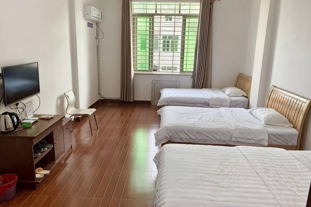 A hotel room with two beds, a desk with a TV, and a window with curtains.
