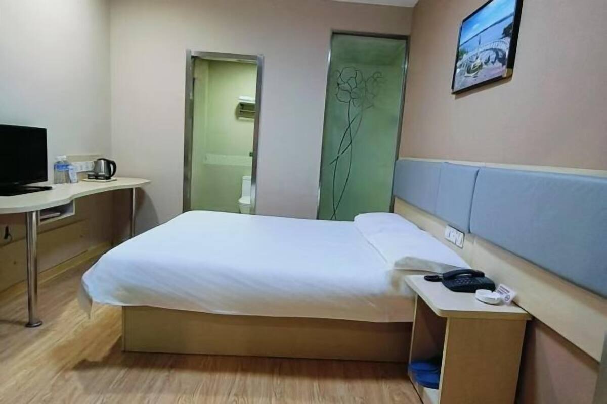 Una habitación de hotel con cama, escritorio, teléfono, televisión y espejo.