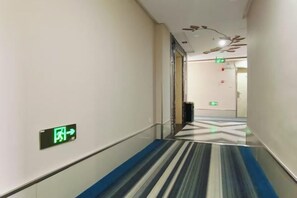 Un couloir d’hôtel avec un tapis à rayures, une rambarde en verre et un panneau indiquant la sortie de secours.