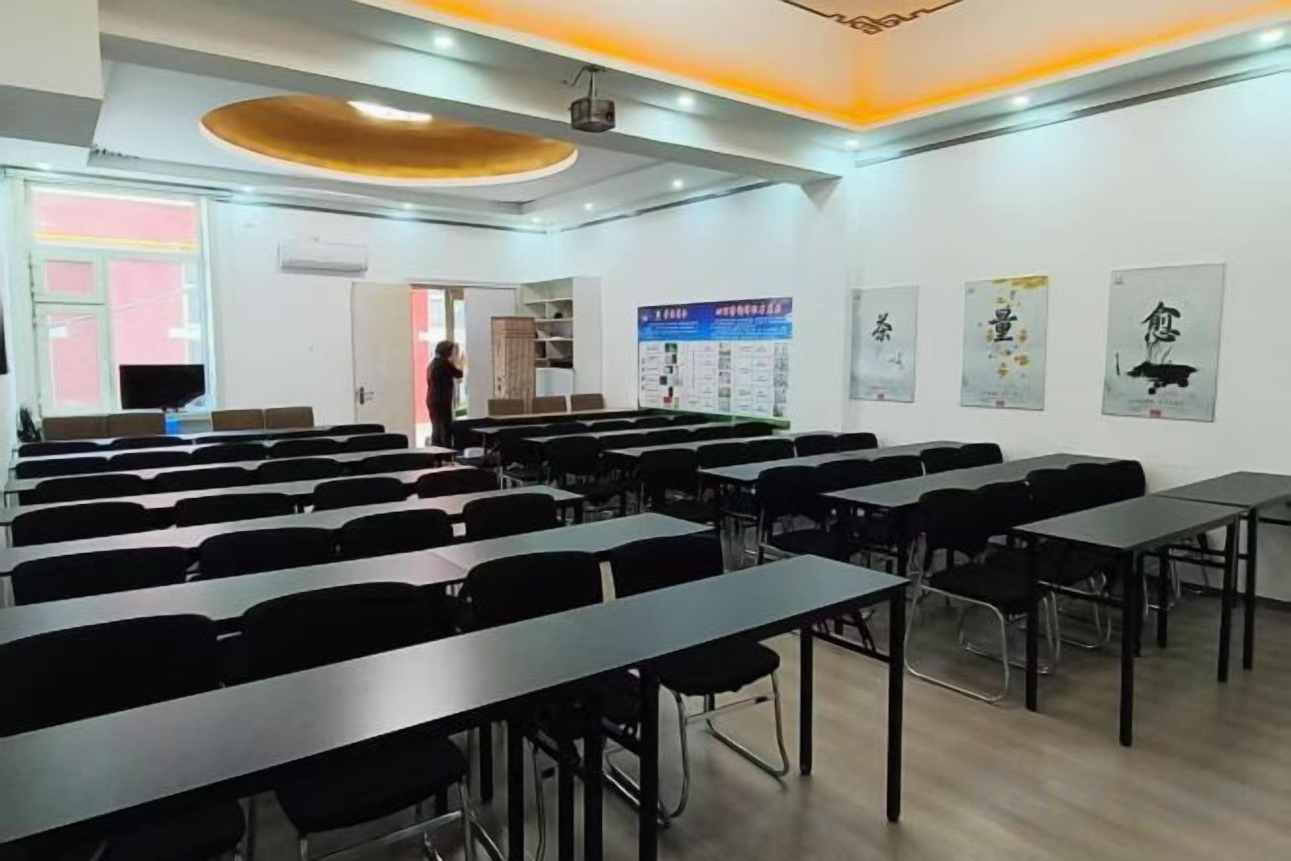 Un aula con filas de mesas y sillas, un proyector y carteles educativos en las paredes.