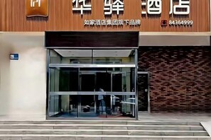 A hotel entrance with a glass door and a brick wall backdrop. - Huayi Hotel (Harbin CapitaLand Airport Bus Station) (Harbin)
