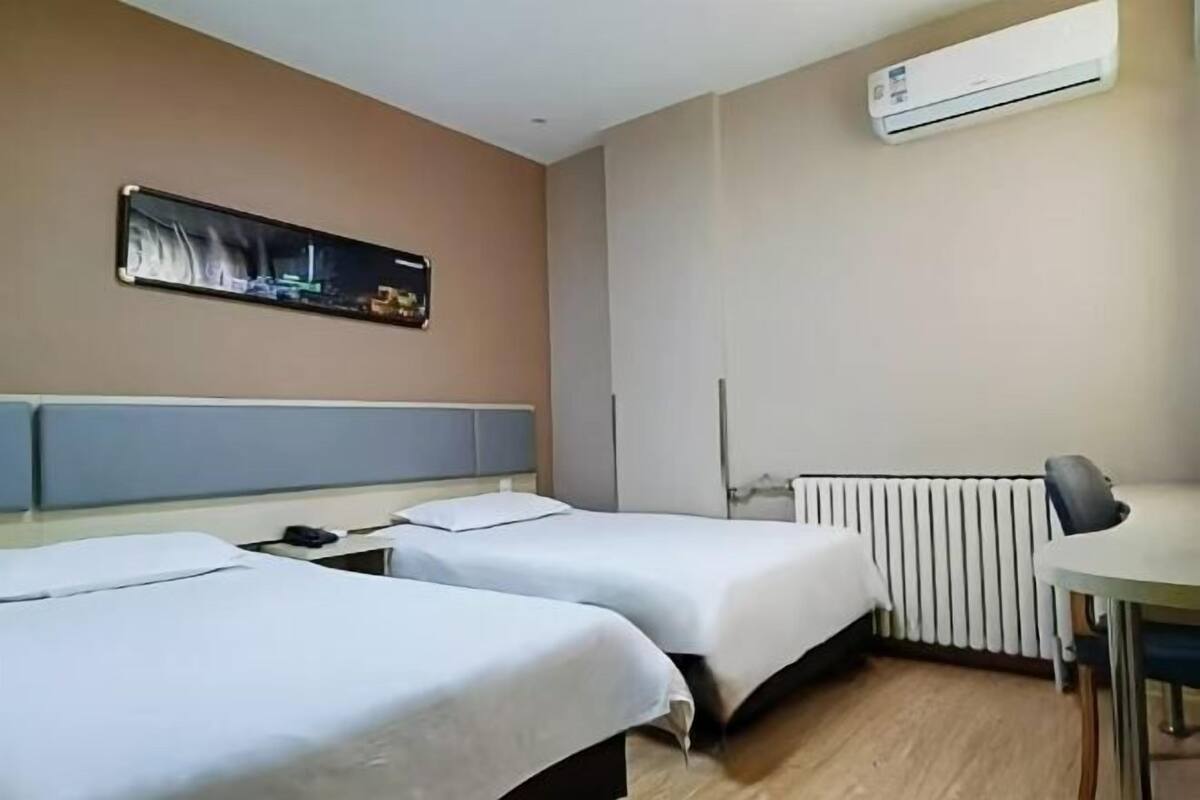 Una habitación de hotel con dos camas, un escritorio, aire acondicionado y un televisor montado en la pared.