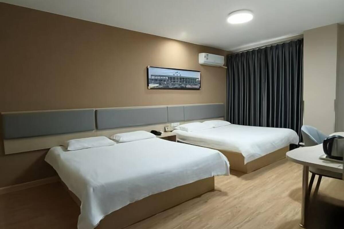 Habitación de hotel con dos camas, un escritorio, una silla, un cuadro en la pared y un equipo de aire acondicionado.