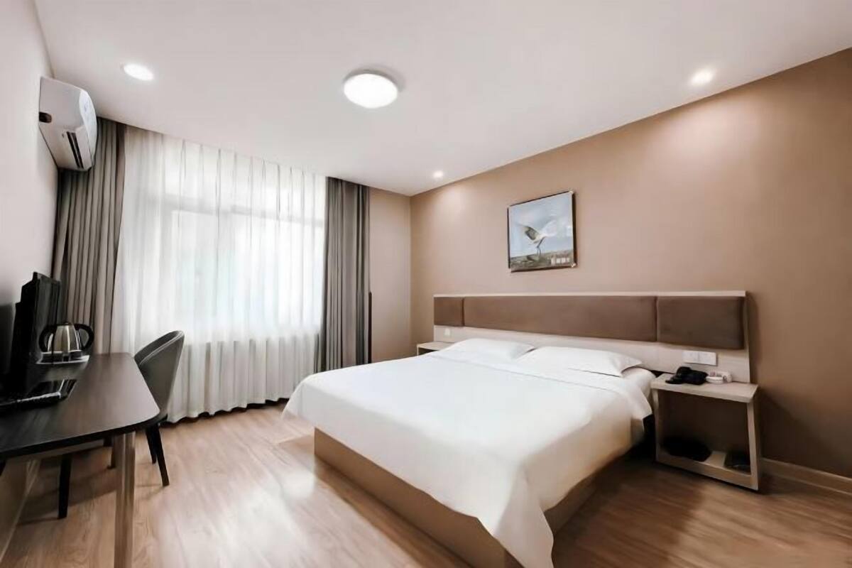 Una habitación de hotel con cama, escritorio, silla, televisor y aire acondicionado.