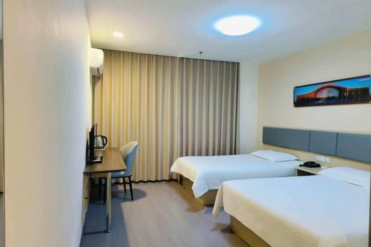 Habitación de hotel con dos camas individuales, un escritorio con silla, una cafetera y un cuadro en la pared.