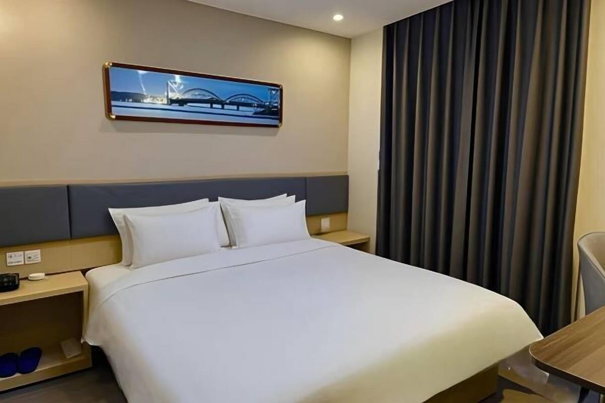 Habitación de hotel con una cama grande, una mesita de noche, una silla y una ventana con cortinas.