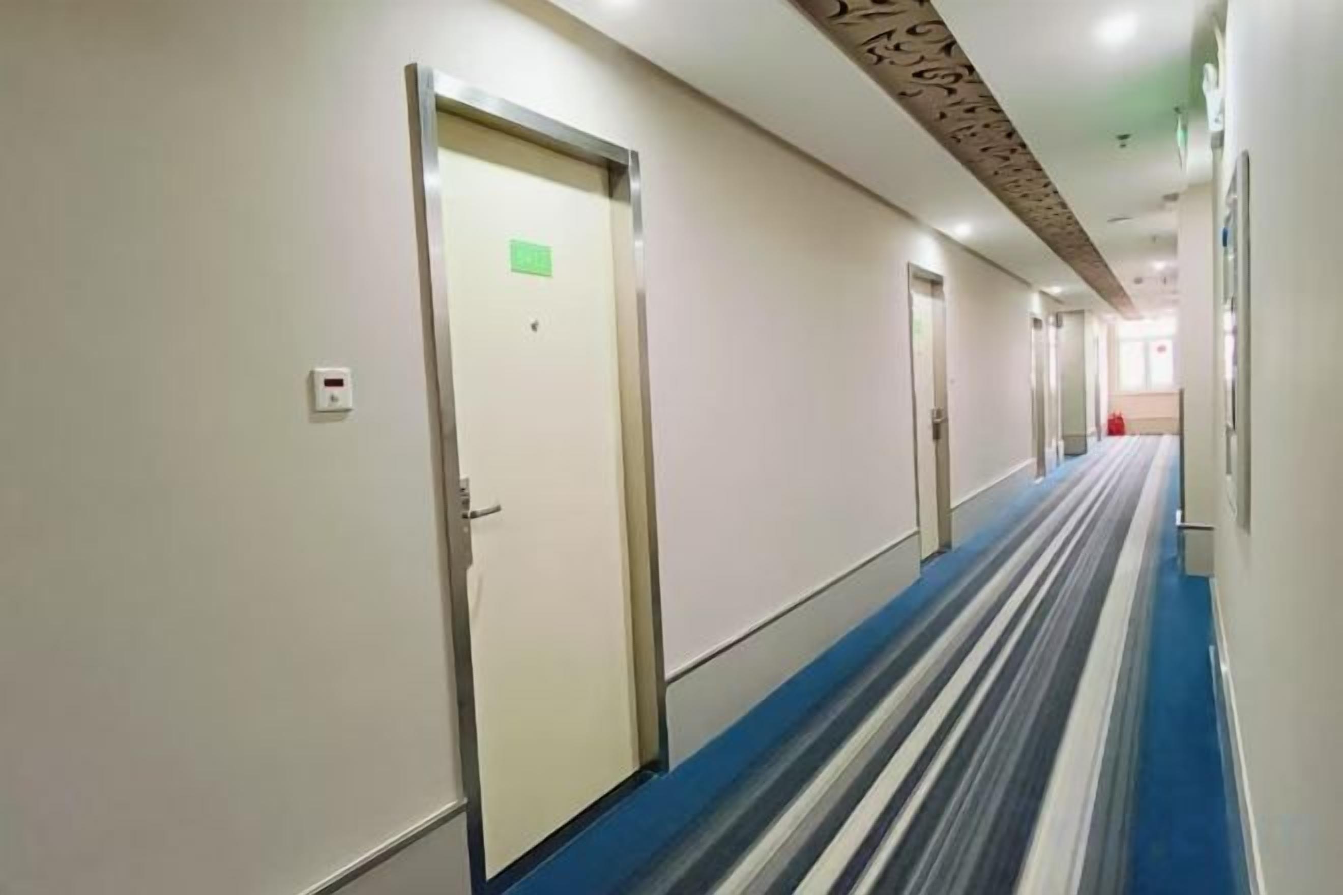 A hotel corridor with doors, a blue carpet, and a ceiling with a light fixture.