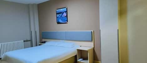 Una habitación de hotel con cama, mesita de noche y televisor montado en la pared.