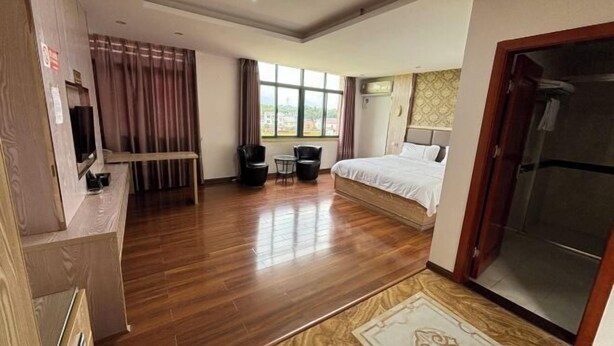 A hotel room with a wooden floor, a bed with white bedding, a desk with a chair, a small table with two chairs, and a window with curtains. - Andes Hotel Pingjiang (Pingjiang)