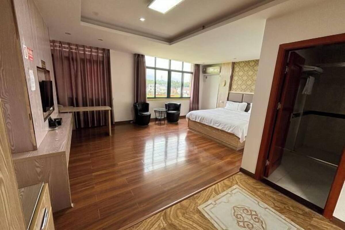 Une chambre d’hôtel avec un plancher en bois, un lit avec une literie blanche, un bureau avec une chaise, une petite table avec deux chaises et une fenêtre avec des rideaux.