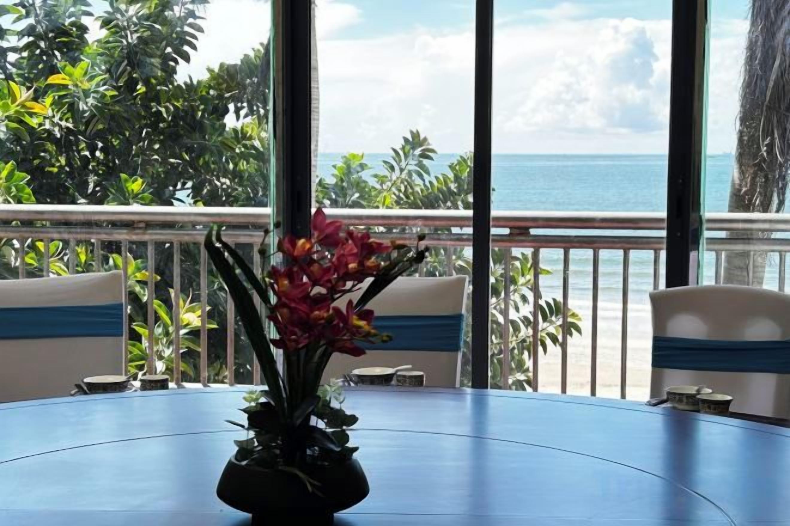 A table with a vase of flowers, a view of the ocean, and a balcony with a railing.