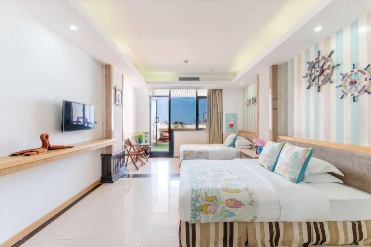 Habitación de hotel con dos camas, televisión, escritorio y vista al mar.