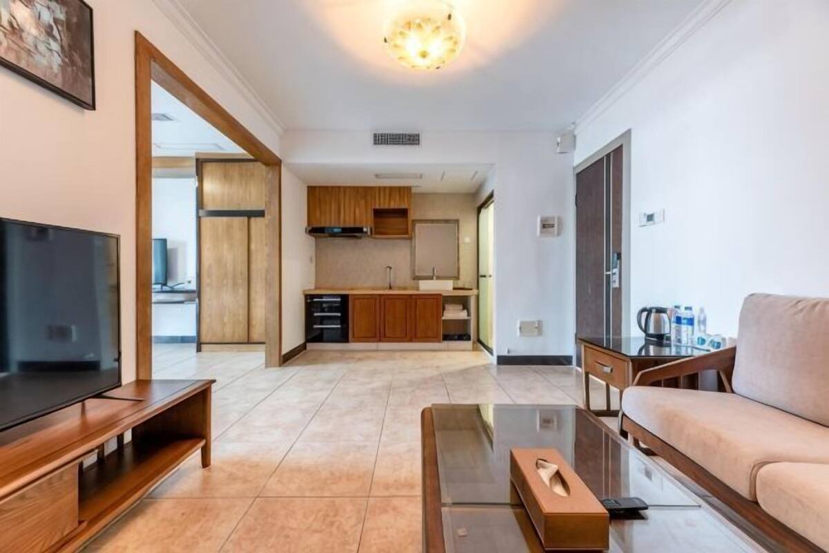 Una sala de estar moderna con televisor, sofá, mesa de centro y una cocina al fondo.