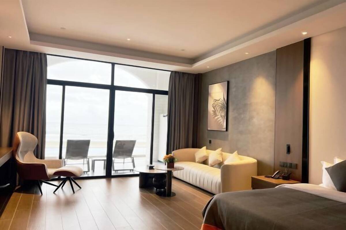 Una habitación de hotel moderna con un ventanal grande, un sofá, una cama, un escritorio y una silla.