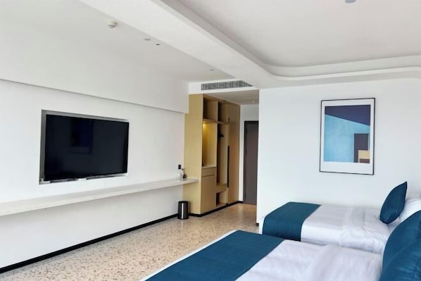 A modern hotel room with a flat-screen TV mounted on the wall, a bed with blue bedding, and a framed abstract painting. - Shenzhen-Shantou Special Cooperation Zone Nanfangao Fishing Port Resort (Haifeng)