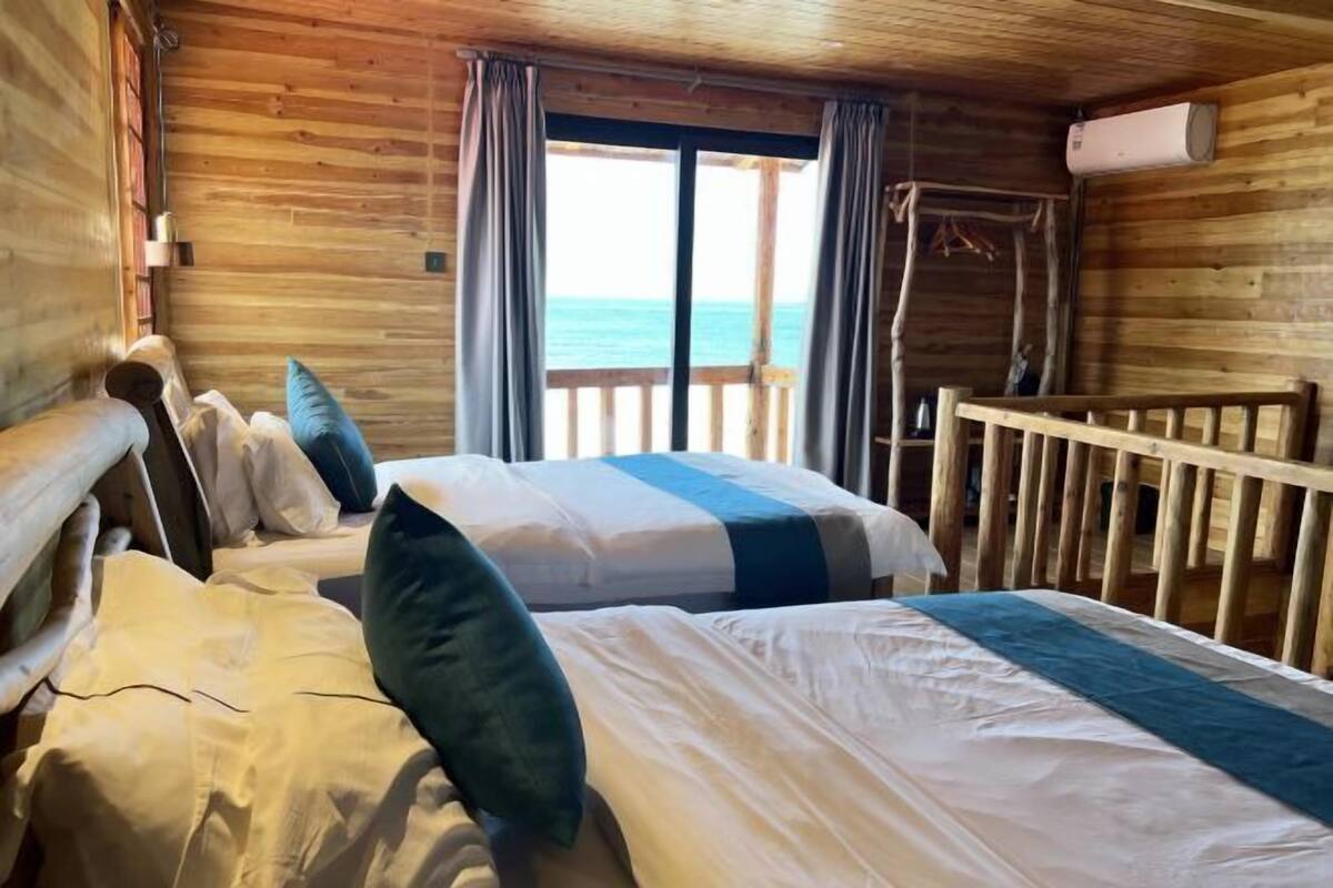 Habitación de cabaña de madera con dos camas, un balcón y un aire acondicionado.