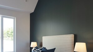 A bedroom with a bed, two bedside tables with lamps, a window, and a dark wall.