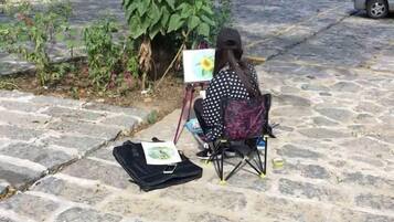 A person seated on a chair with a painting on a stand, a bag on the ground, and a plant nearby.