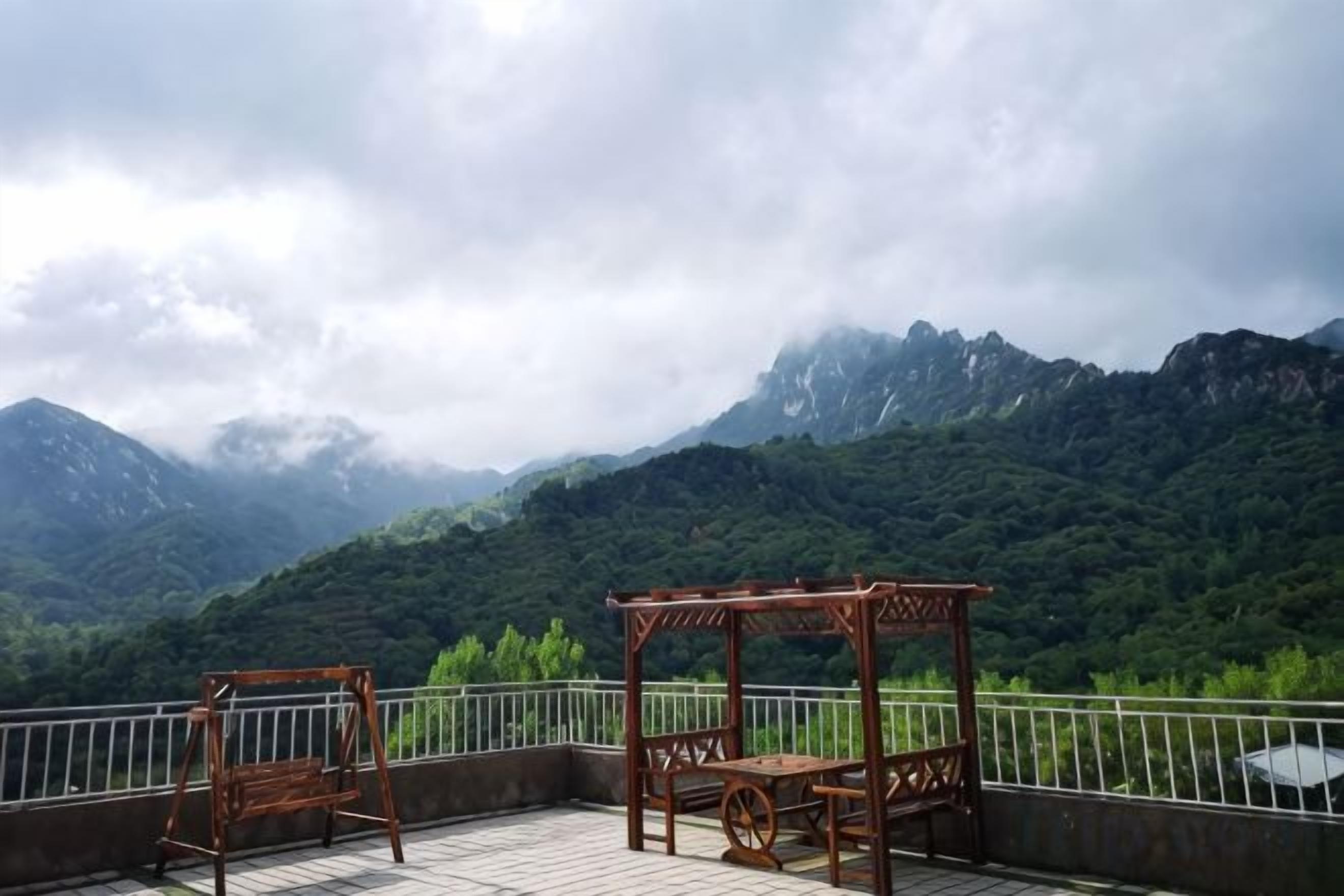 A balcony with a view of mountains, a wooden swing, and a table.