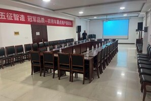 A conference room with a long table, chairs, a projector screen, and a banner on the wall. - Monkey Mountain Villa Hotel (Mengyin)