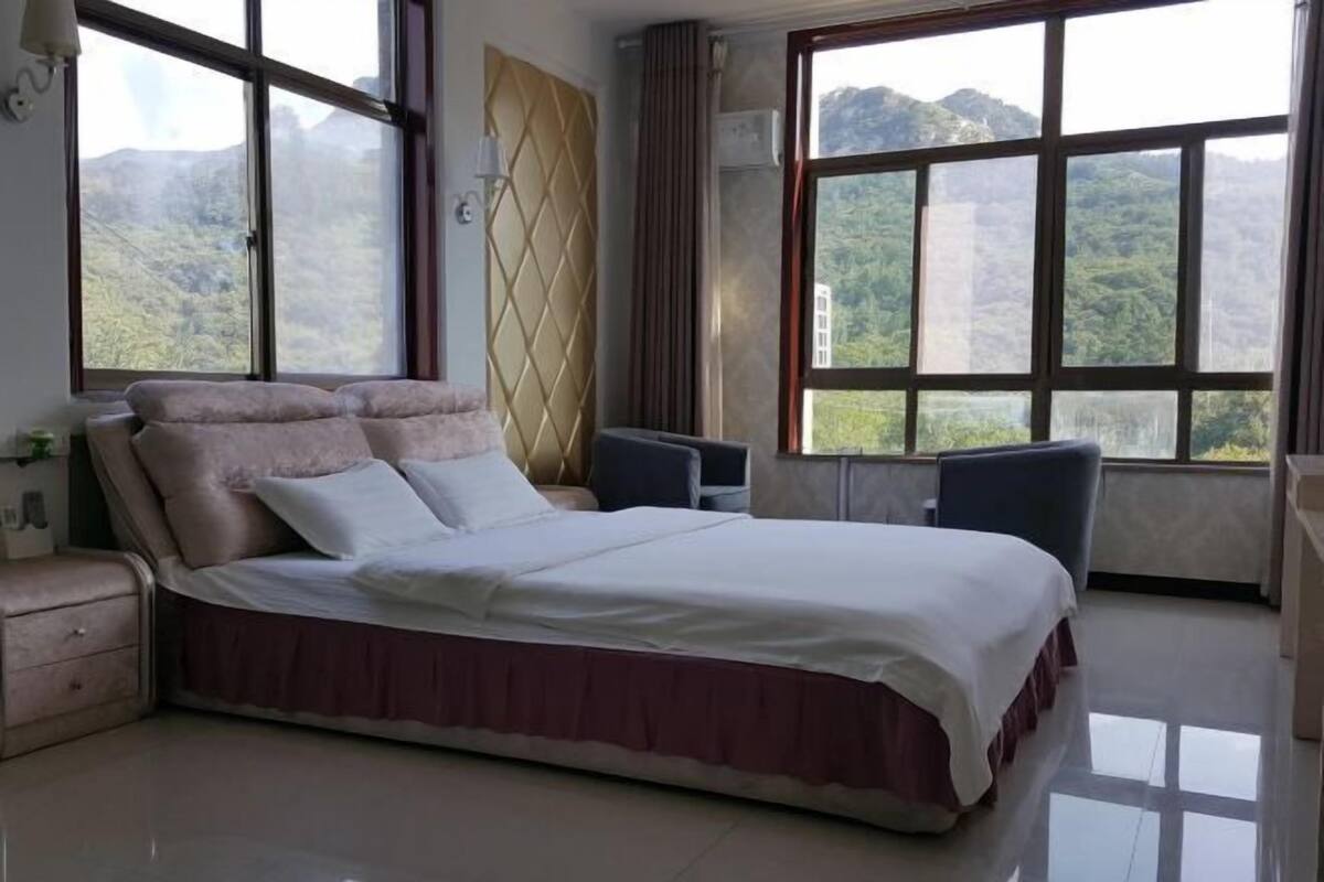 Habitación de hotel con una cama grande, un escritorio y vistas a montañas a través de amplios ventanales.
