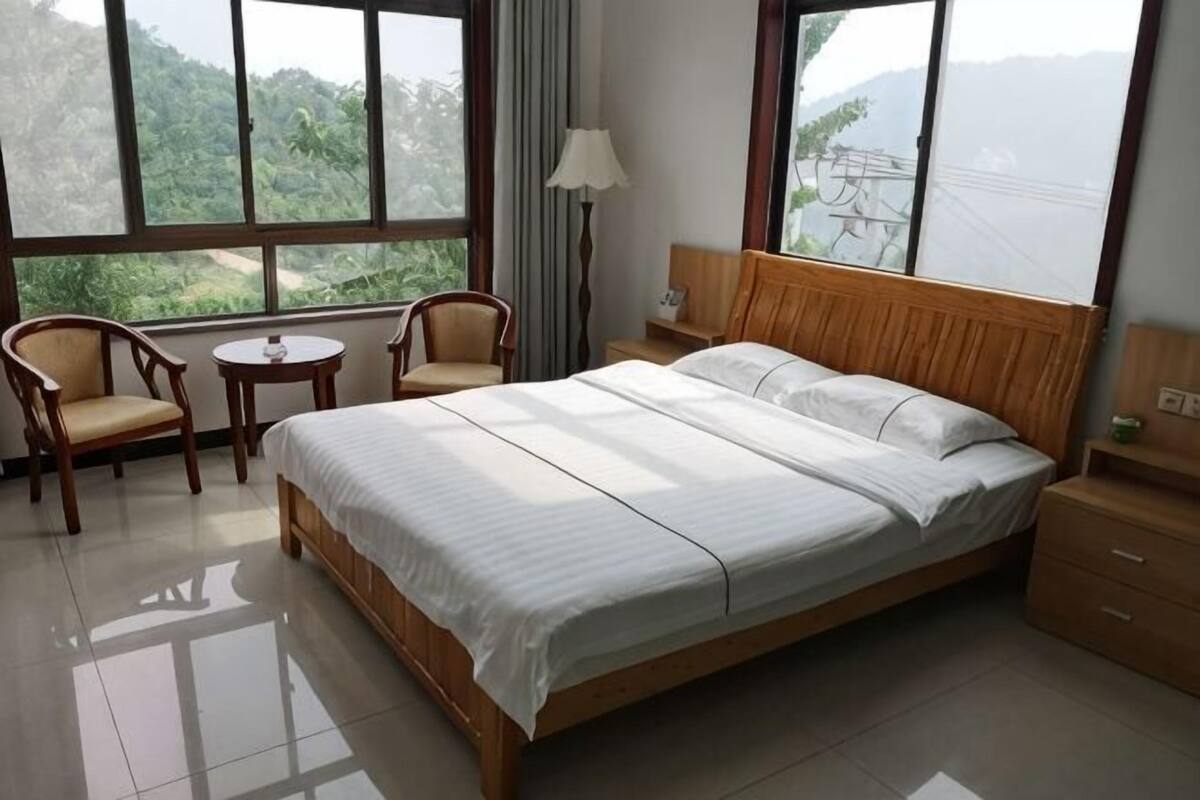 Habitación de hotel con una cama grande, dos sillas, una mesita, una mesita de noche y una ventana con vistas a zonas verdes.