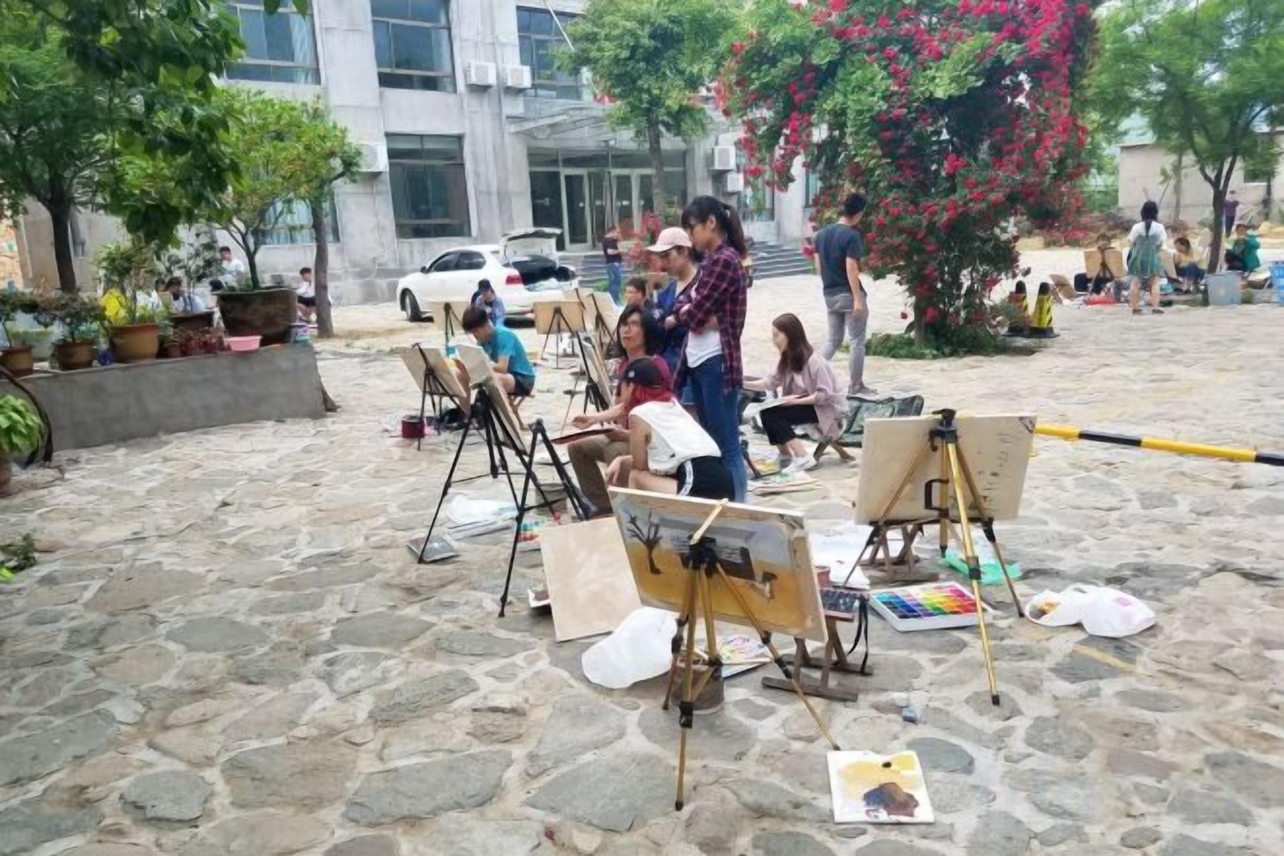 An outdoor art class with easels and canvases set up on a cobblestone surface.