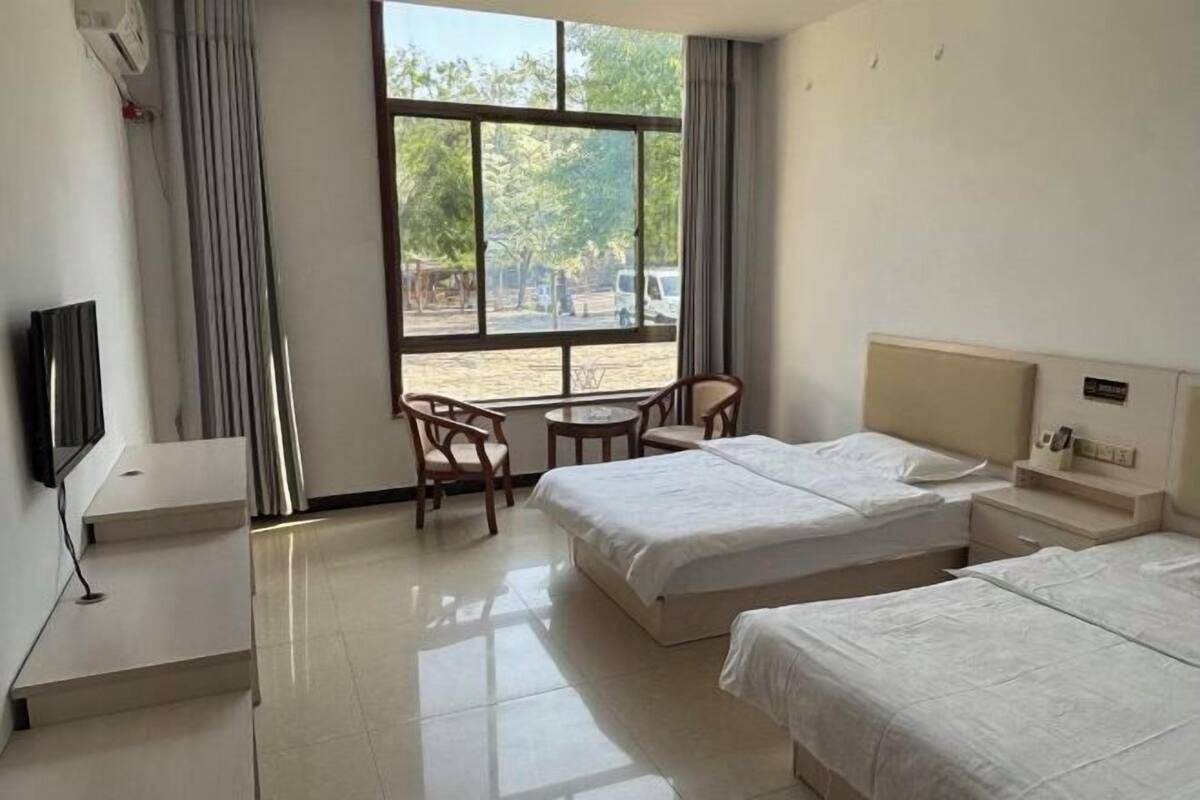 Habitación de hotel con dos camas, televisión, escritorio, silla y ventana con vista al exterior.