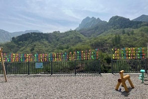 A gravel area with a wooden sculpture, a metal fence, and a view of green mountains.