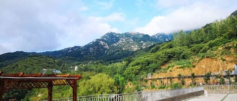 Una terraza con estructura de madera, un contenedor de basura verde y vista a una cordillera.