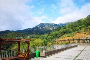 Una terrazza con struttura in legno, un cestino verde e vista su una catena montuosa.