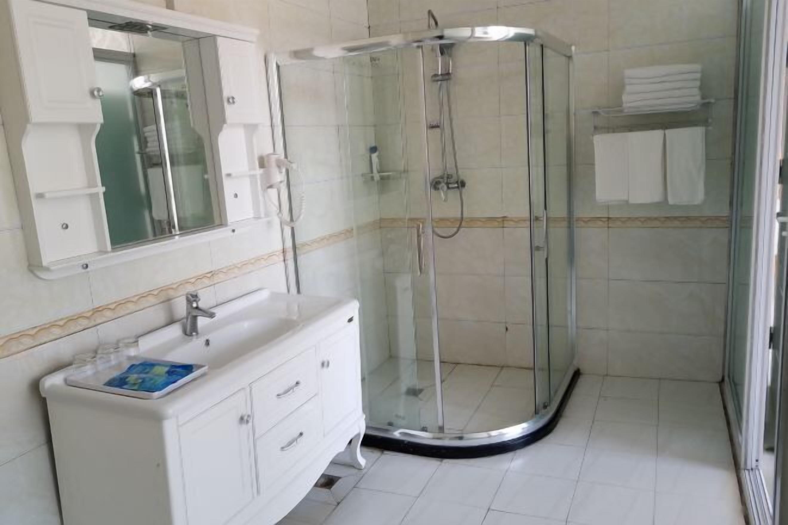 Un baño con ducha envuelta en vidrio, un tocador blanco con espejo y piso de baldosas.