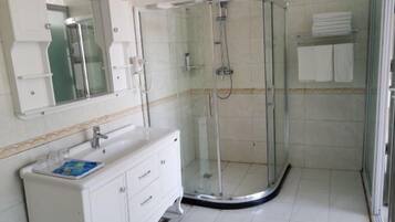 Un baño con ducha envuelta en vidrio, un tocador blanco con espejo y piso de baldosas.